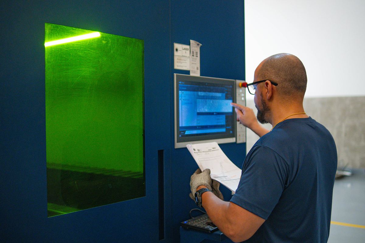 Operador no painel da máquina de corte a laser, com a cabine iluminada em verde